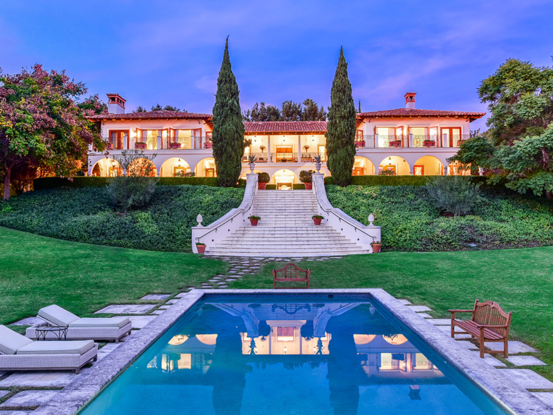 Luxury estate in Rancho Santa Fe, San Diego, featuring a grand Mediterranean-style mansion with manicured gardens, a large swimming pool, and elegant landscaping, highlighted during a vibrant sunset.